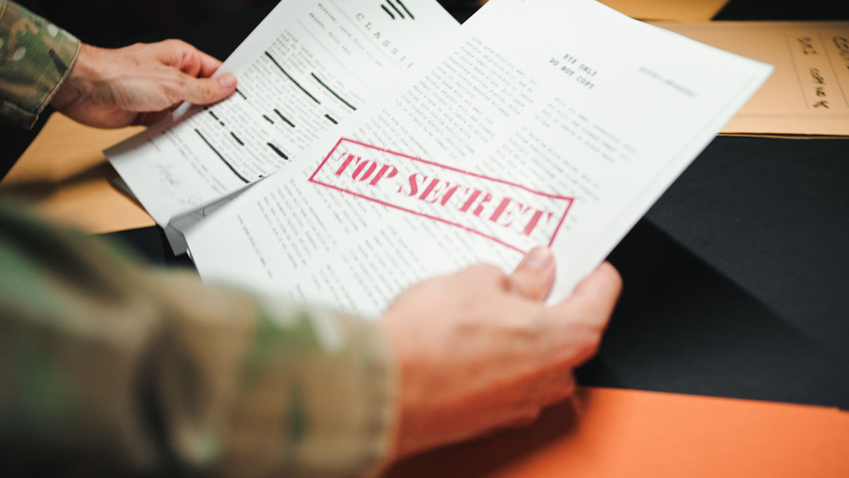 A person in military uniform is examining a document stamped with 'TOP SECRET' across the front.