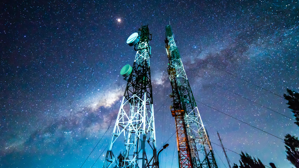 A communication tower silhouetted against a starry night sky with the Milky Way galaxy visible in the background.