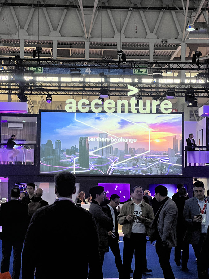 A crowded Accenture exhibit with a large screen reading 'Let there be change' above the audience.