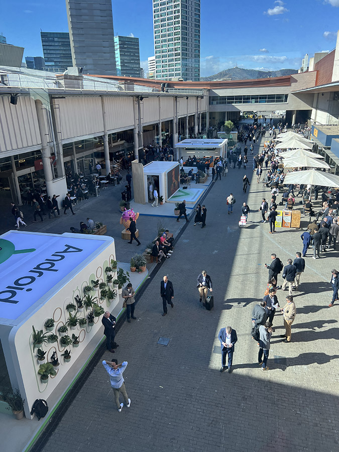 An overhead view of a busy outdoor courtyard at a conference with attendees milling around various booths and seating areas.