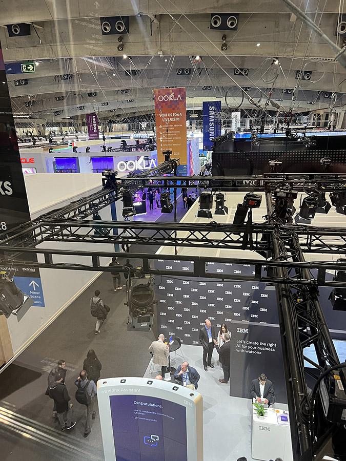 An indoor upper-level view of a trade show floor with event production equipment overlooking various company booths.