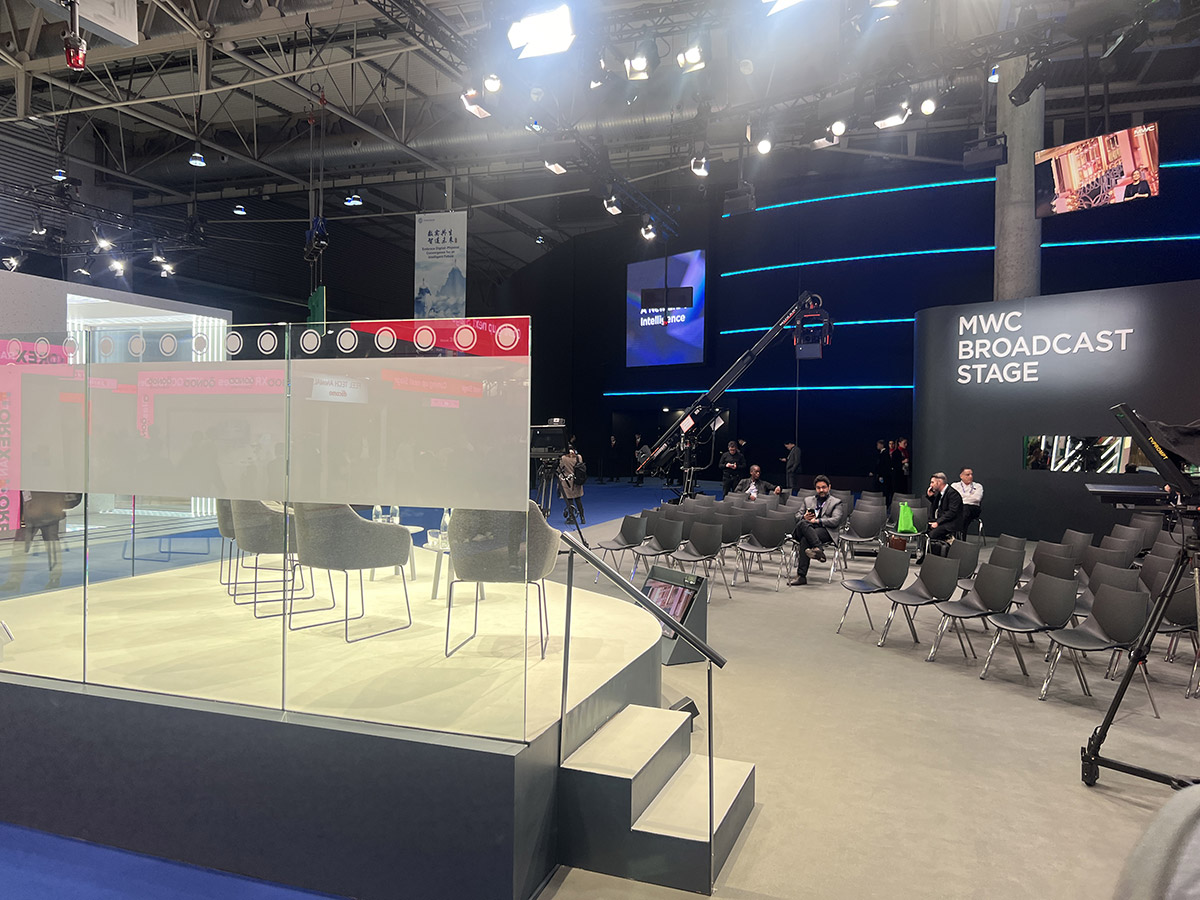 The MWC Broadcast Stage set up with chairs and a clear partition, ready for an event, with few attendees seated.
