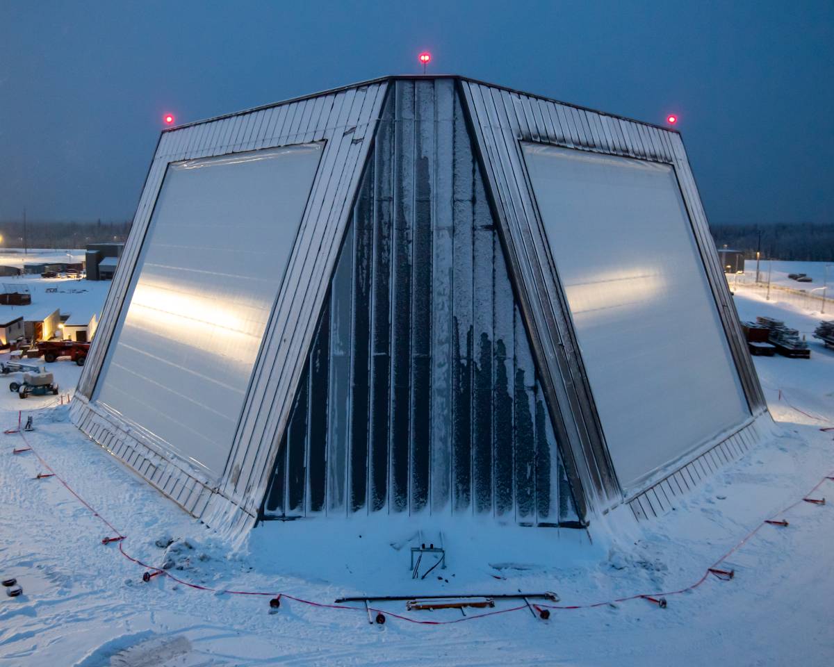 A snow-covered Long Range Discrimination Radar (LRDR) at Clear Space Force Station, Alaska, featuring a distinctive angular, metallic structure with red warning lights, as seen in the twilight.