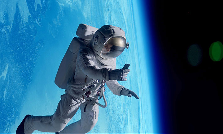 An astronaut in a space suit is engaging in a video call on her mobile phone while floating in space with the Earth visible in the background.