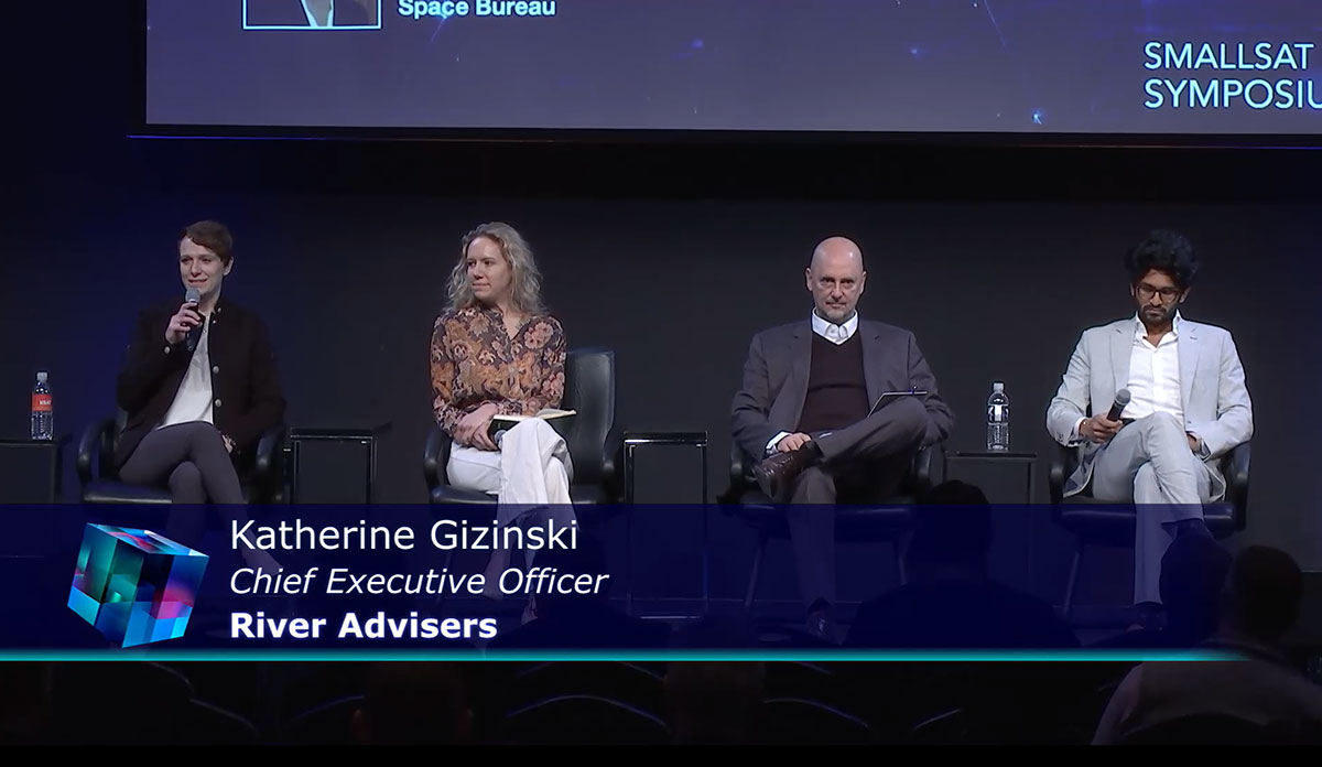 Four professionals are seated on stage at the SmallSat Symposium, engaged in a panel discussion.