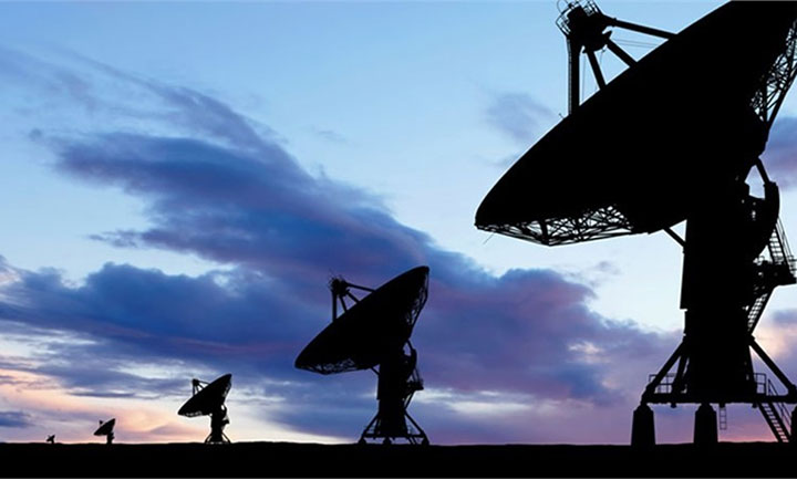 Silhouettes of large satellite dishes against a dusk sky with shades of blue and purple, with the dishes positioned at different angles.