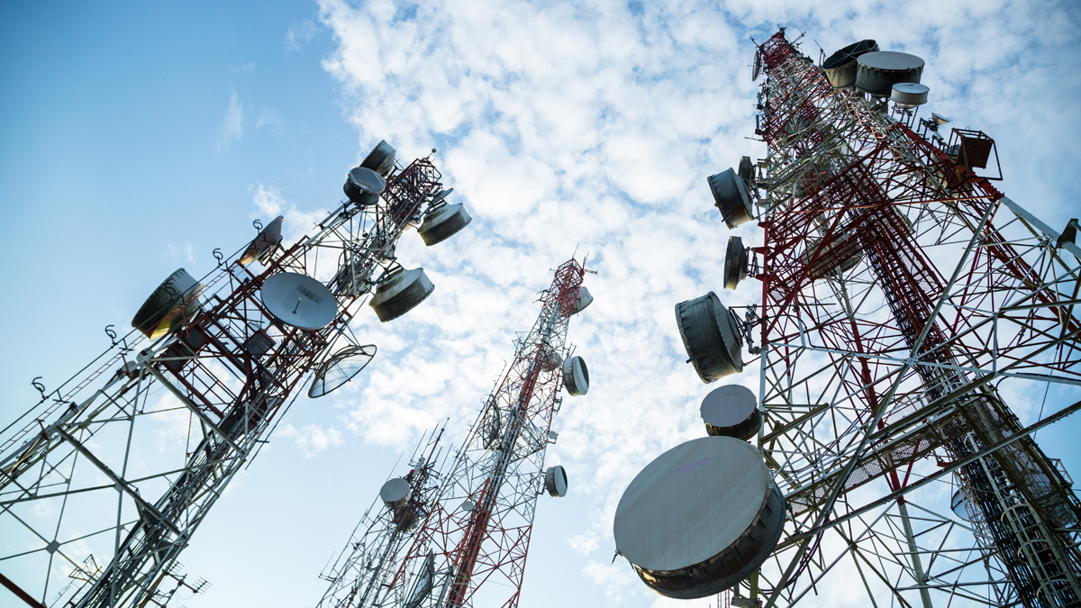 Multiple telecommunication masts with various TV antennas and wireless technology equipment against a blue sky with morning clouds.