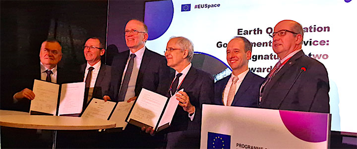 A group of six senior officials from various European organizations, smiling and holding up signed study contracts in front of a podium with the #EUSpace backdrop, after a contract signing event for a European Union Earth observation governmental service.