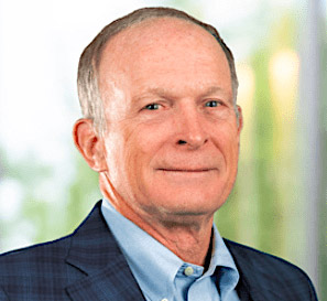 A portrait of Paul Gaske wearing a blue suit, light blue shirt, and blue tie, in front of a blurred background.