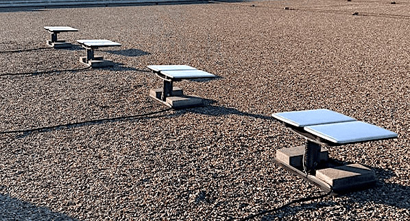 A series of four rectangular, flat-panel satellite antennas mounted on a flat rooftop covered in gravel.