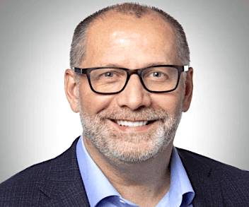 A portrait of a smiling man with glasses, a beard, and wearing a business suit.