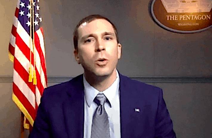 A man in a blue suit and tie speaking, with the American flag and the Pentagon seal in the background.