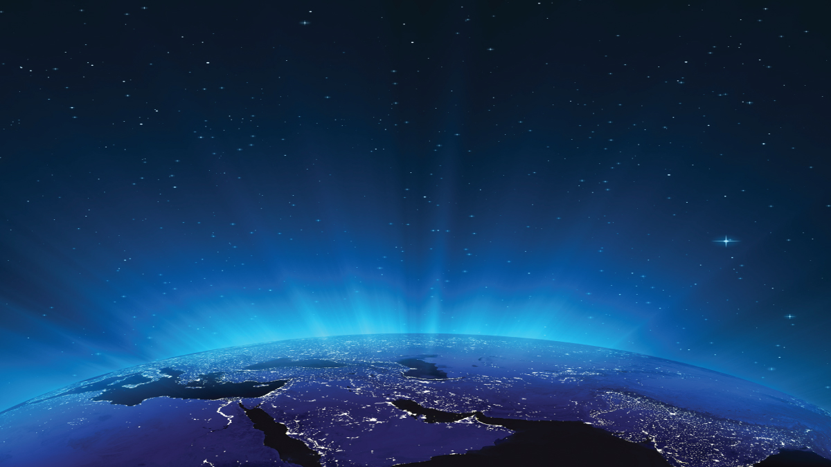 View of Earth from space at night, with glowing city lights, a blue atmospheric haze, and a star-filled sky.