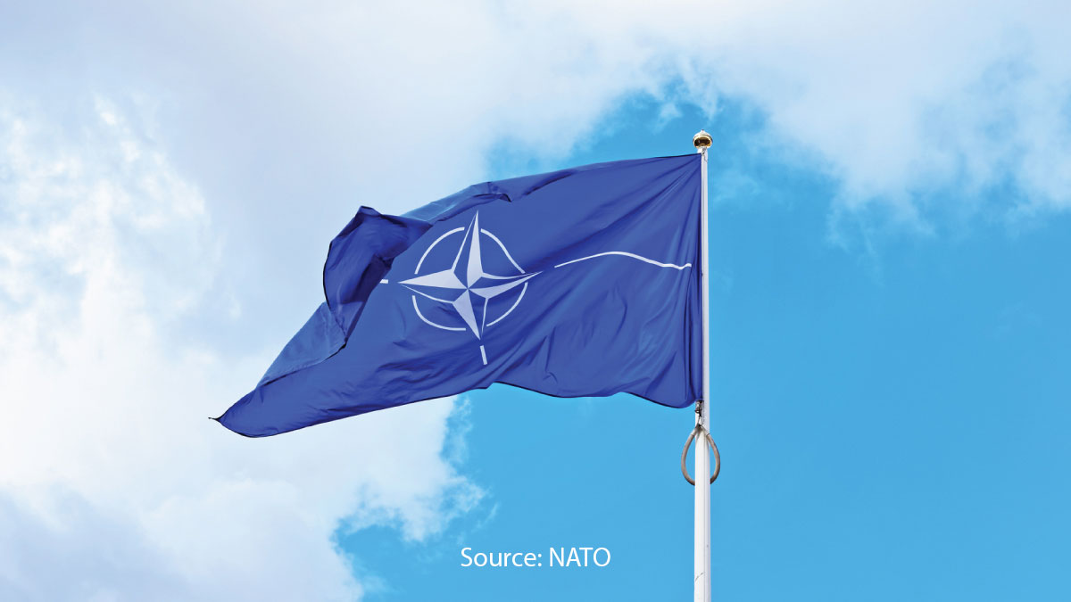 The flag of the North Atlantic Treaty Organization (NATO) waving against a bright, partly cloudy sky. (Source: NATO)