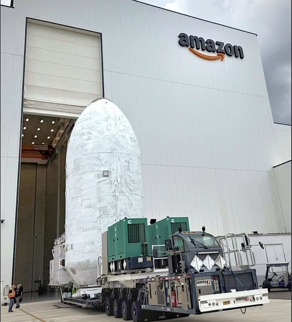 Rocket payload fairing carrying Project Kuiper satellites on a transport vehicle outside an Amazon satellite processing facility.