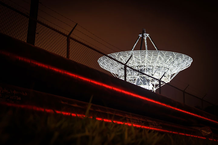 Satellite dish behind barbed wire with laser security protection.