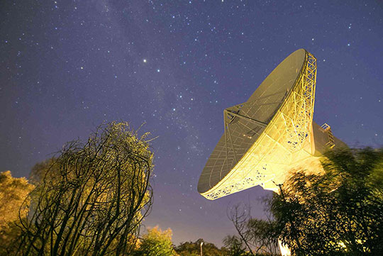 The 35 m-diameter dish antenna of ESA's deep-space tracking station at New Norcia, Australia, illuminated by ground lights against the night sky